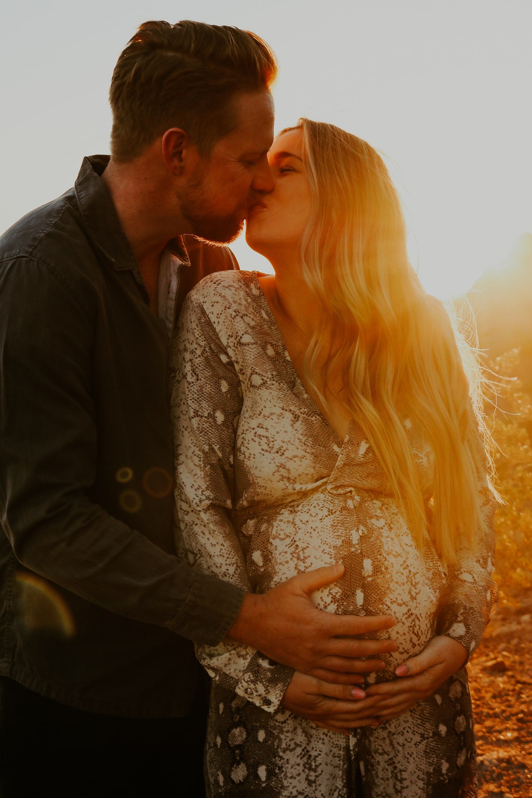 Expecting couple kisses in warm desert backlight, hands on the bump